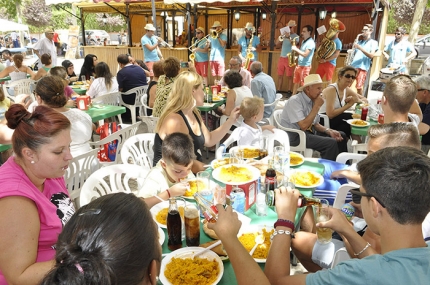 Una familia degusta el arroz popular en  la feria de mediodía con la charanga de fondo 